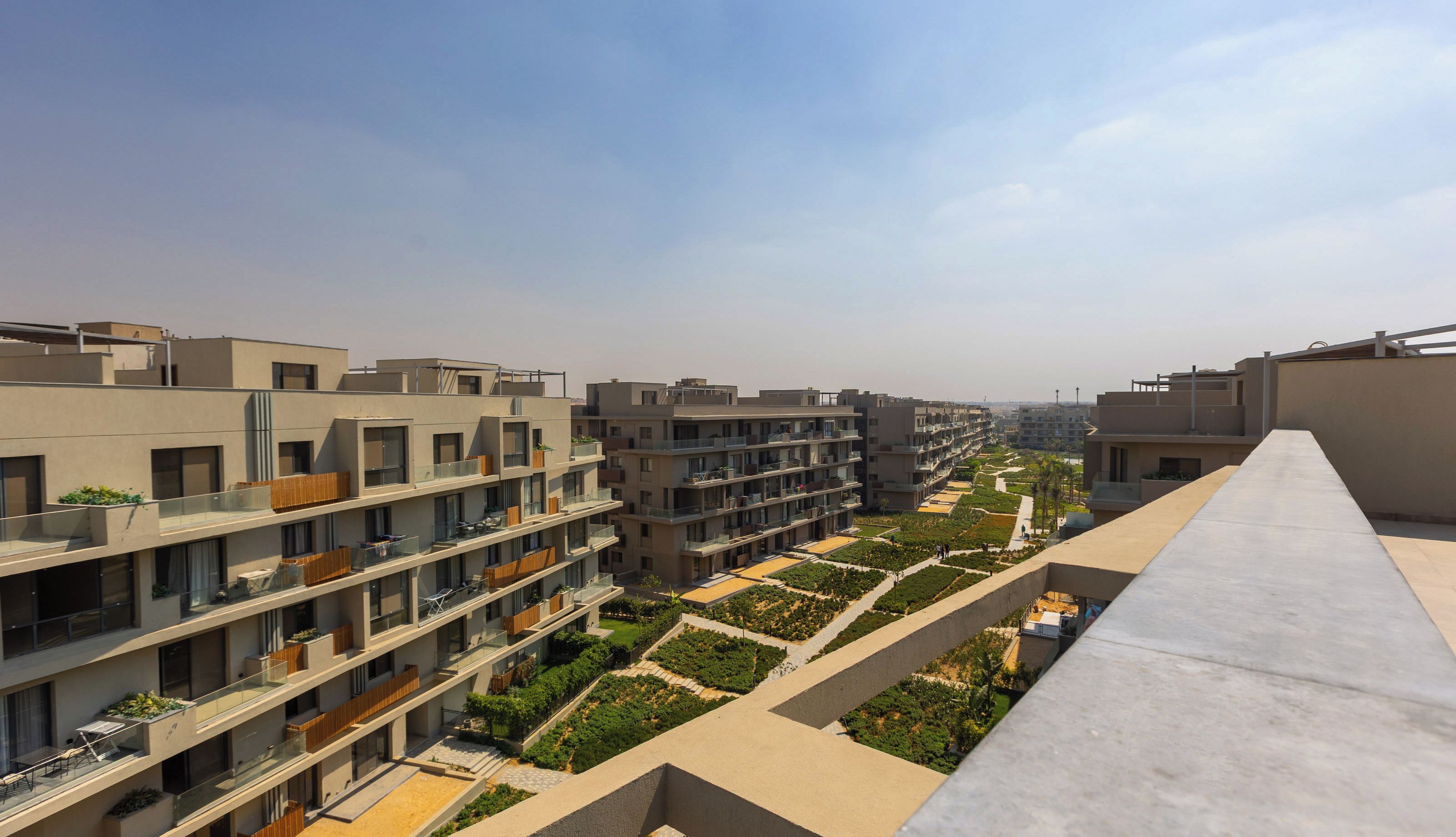 Ein modernes Wohngebäude mit mehreren Balkonen, einer Dachterrasse und einem angelegten Garten.