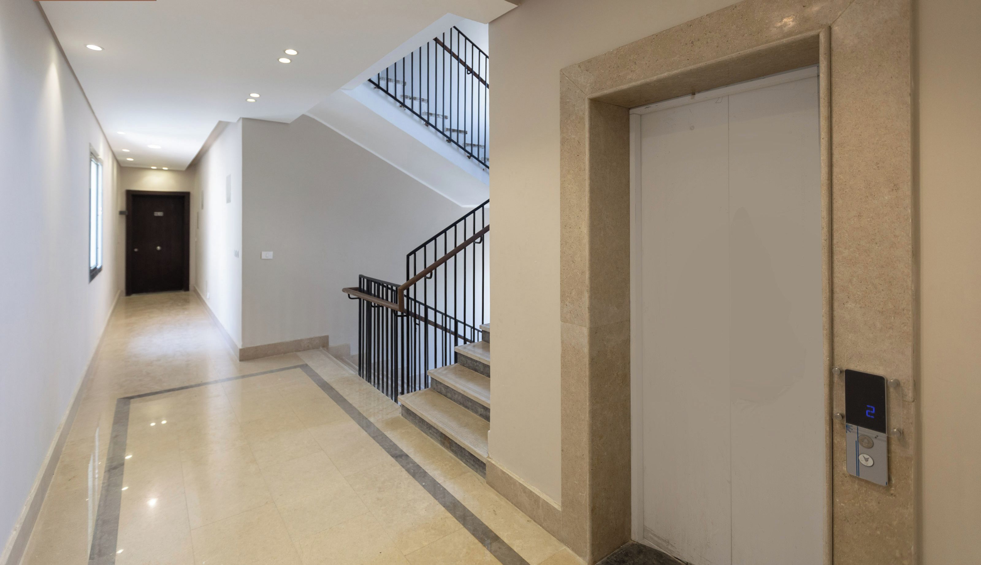 Ein moderner Hotelkorridor mit einer Treppe, einer Tür mit digitalem Schloss und einem Flur, der zu einem dunklen Raum führt.