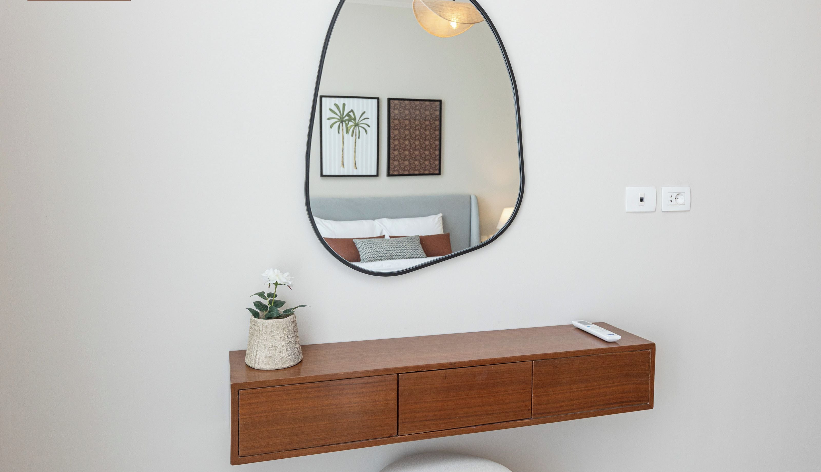 A bathroom with a wooden vanity, a large mirror, a wall-mounted light fixture, and framed artwork.