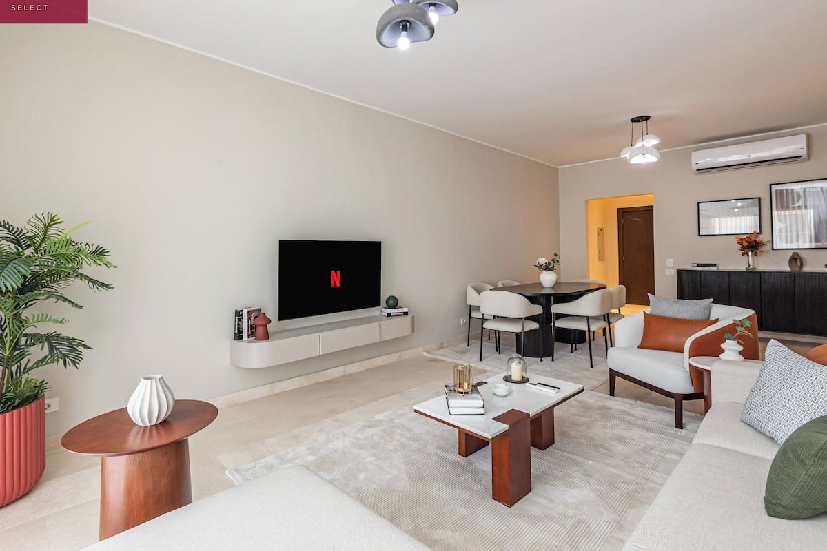 Un salon moderne doté d’un téléviseur à écran plat, d’un coin repas et d’un espace détente avec un canapé et des fauteuils.