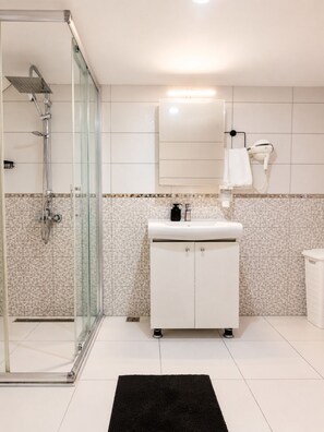 Une salle de bain moderne avec une douche à parois de verre, un meuble-lavabo blanc avec un miroir et un sÚche-cheveux fixé au mur.