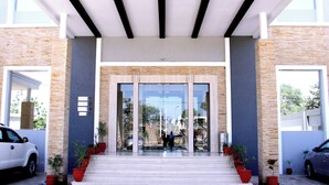 A modern building entrance with a glass door, potted plants, and a staircase leading up to the door.