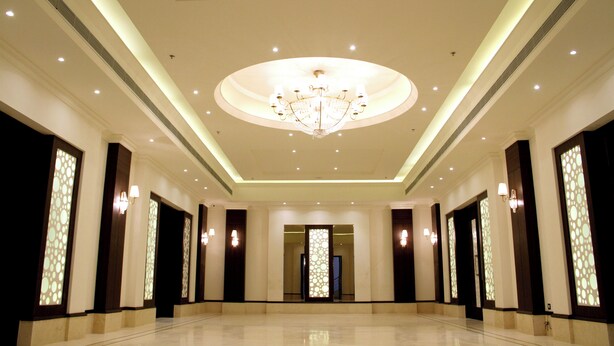 A spacious hotel lobby with a large chandelier, recessed lighting, and decorative wall panels.