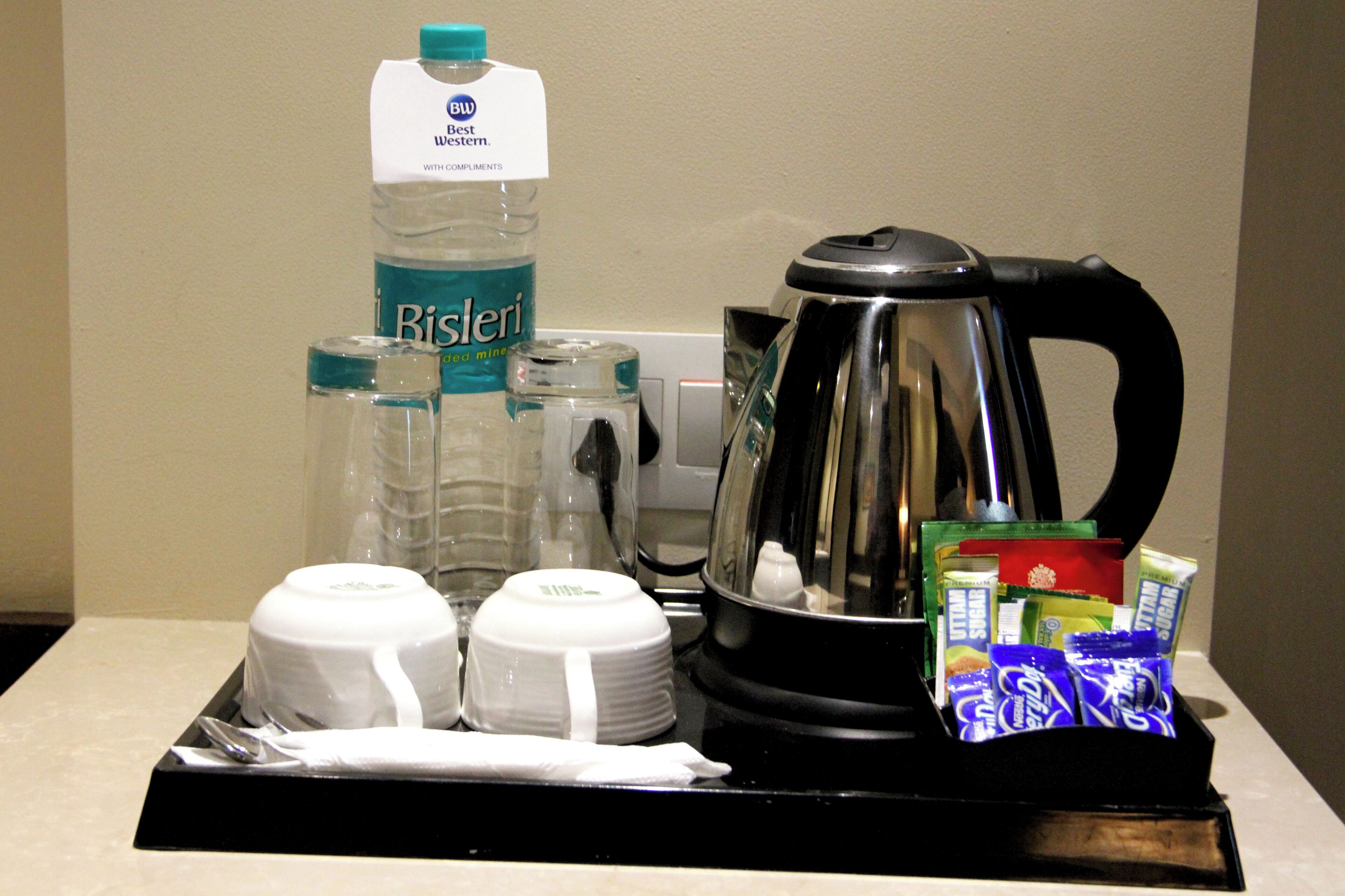 A tray with a coffee pot, water bottle, glasses, and food packets.