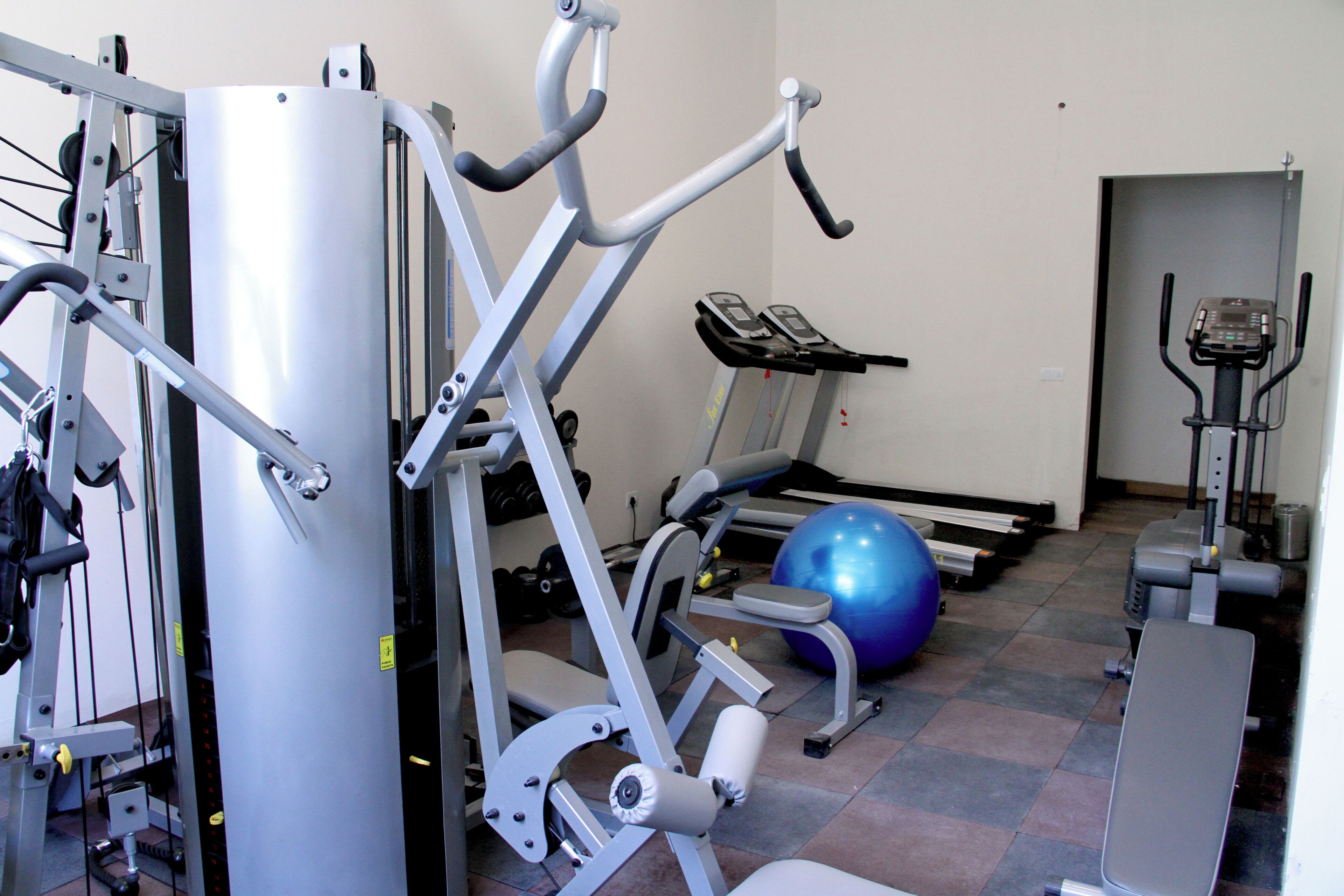 Un gimnasio con equipamiento de ejercicio, una cinta de correr y una pelota de gimnasia azul.