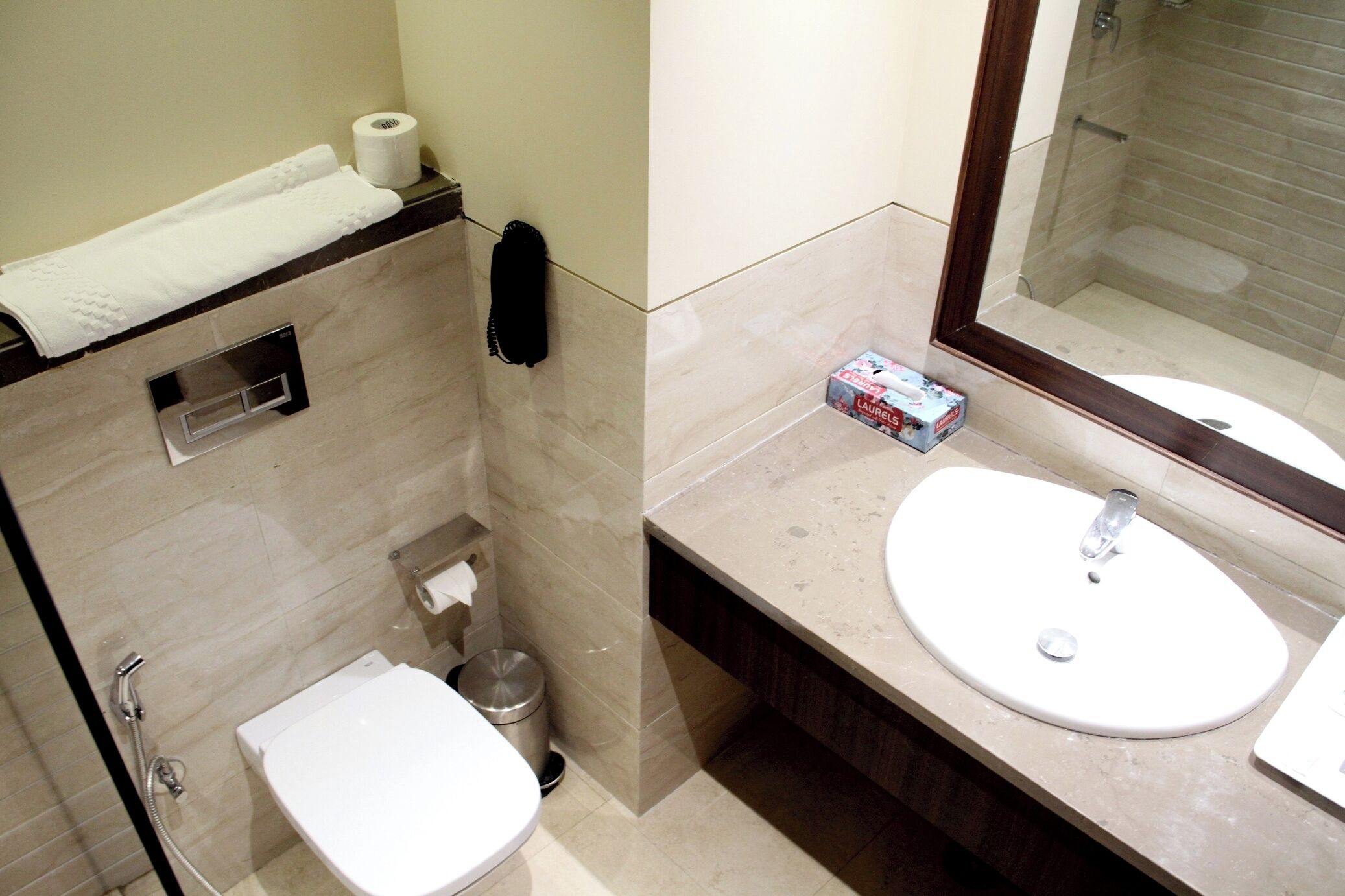 A bathroom with a toilet, sink, and shower. There is a towel rack and a trash can.