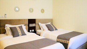 Une chambre d’hôtel avec deux lits, chacun recouvert d’une couverture marron et agrémenté d’oreillers blancs. Des décorations murales sont disposées au-dessus des lits, et une petite table avec une lampe se trouve entre les deux.