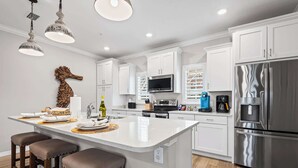 Una cocina moderna con armarios blancos, electrodomésticos de acero inoxidable y una isla central con taburetes de bar.