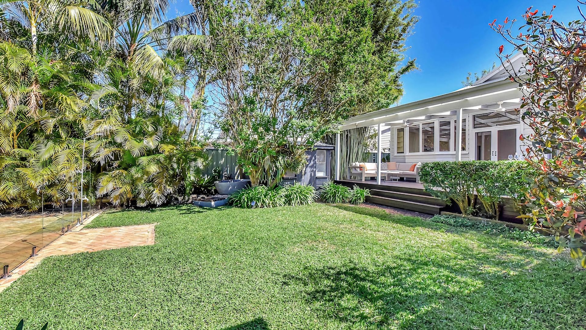 A well-maintained garden with a lawn, various plants, and a modern house with a patio.