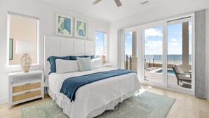 Una camera da letto con un letto, una ventola a soffitto, un'ampia finestra vista mare e un balcone con una sedia.