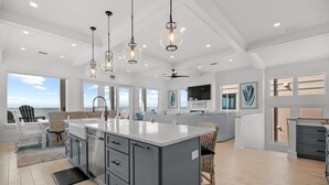Un'ampia cucina con una grande isola, lampade a sospensione moderne e vista sull'oceano.