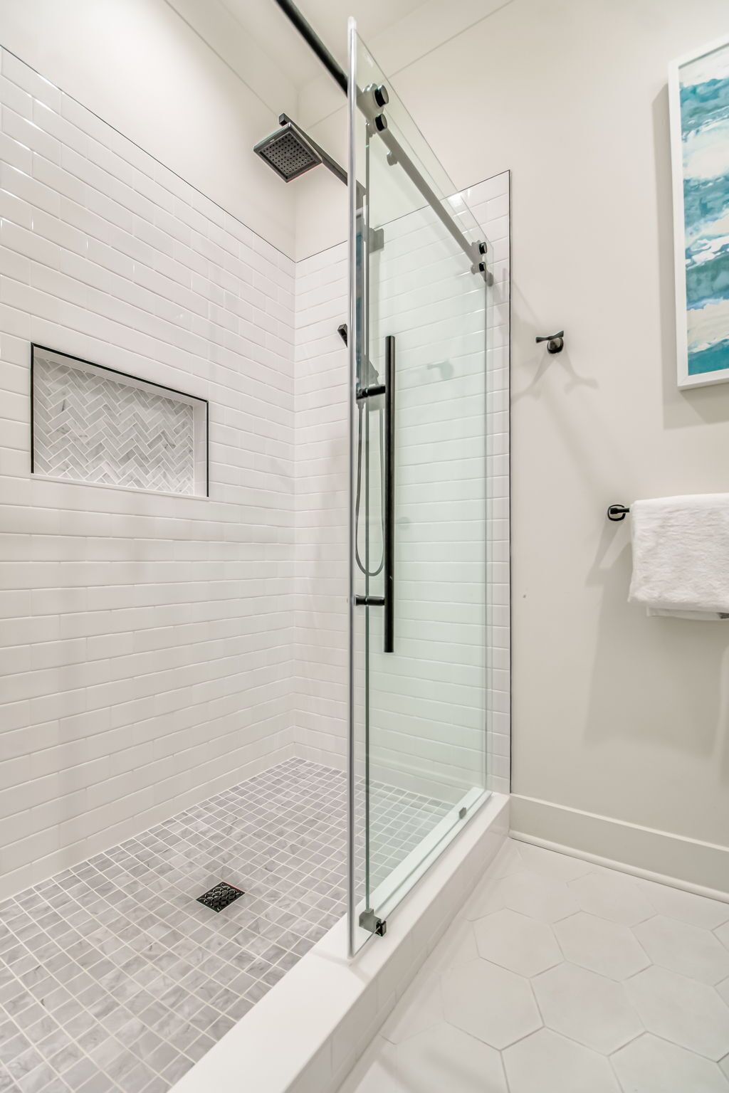 Une douche moderne dotée d’une porte en verre, de murs recouverts de carreaux blancs et d’un sol carrelé en forme d’hexagone.