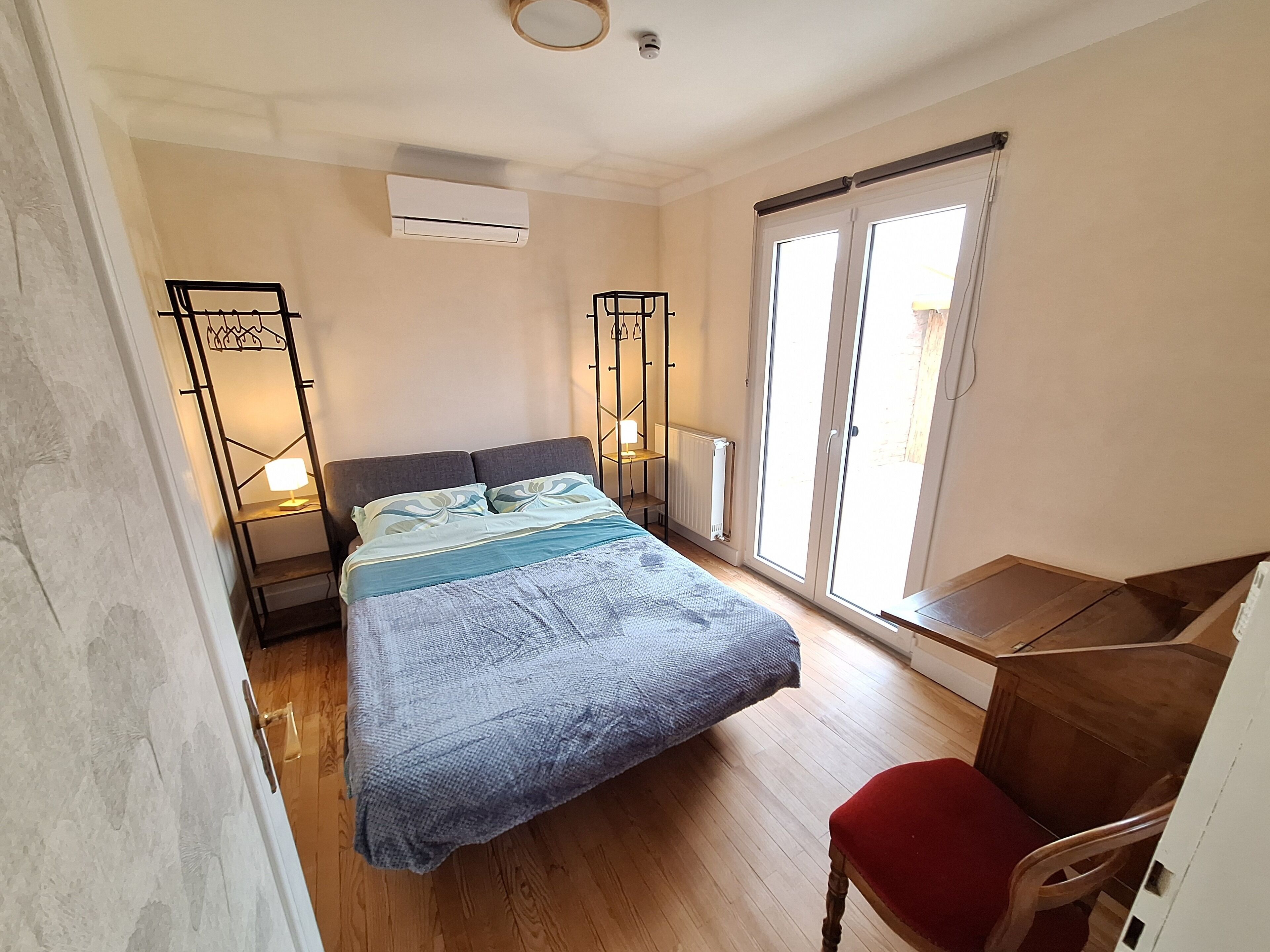 Un dormitorio con cama, escritorio, silla, radiador y ventana con vistas.