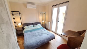 Un dormitorio con cama, escritorio, silla, radiador y ventana con vistas.