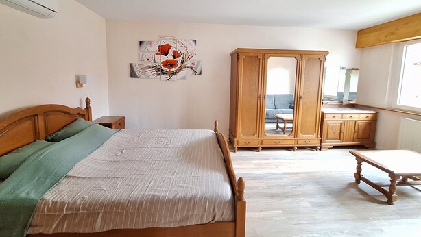 Un dormitorio con una cama de madera, un armario, un banco y una obra de arte colgada en la pared.