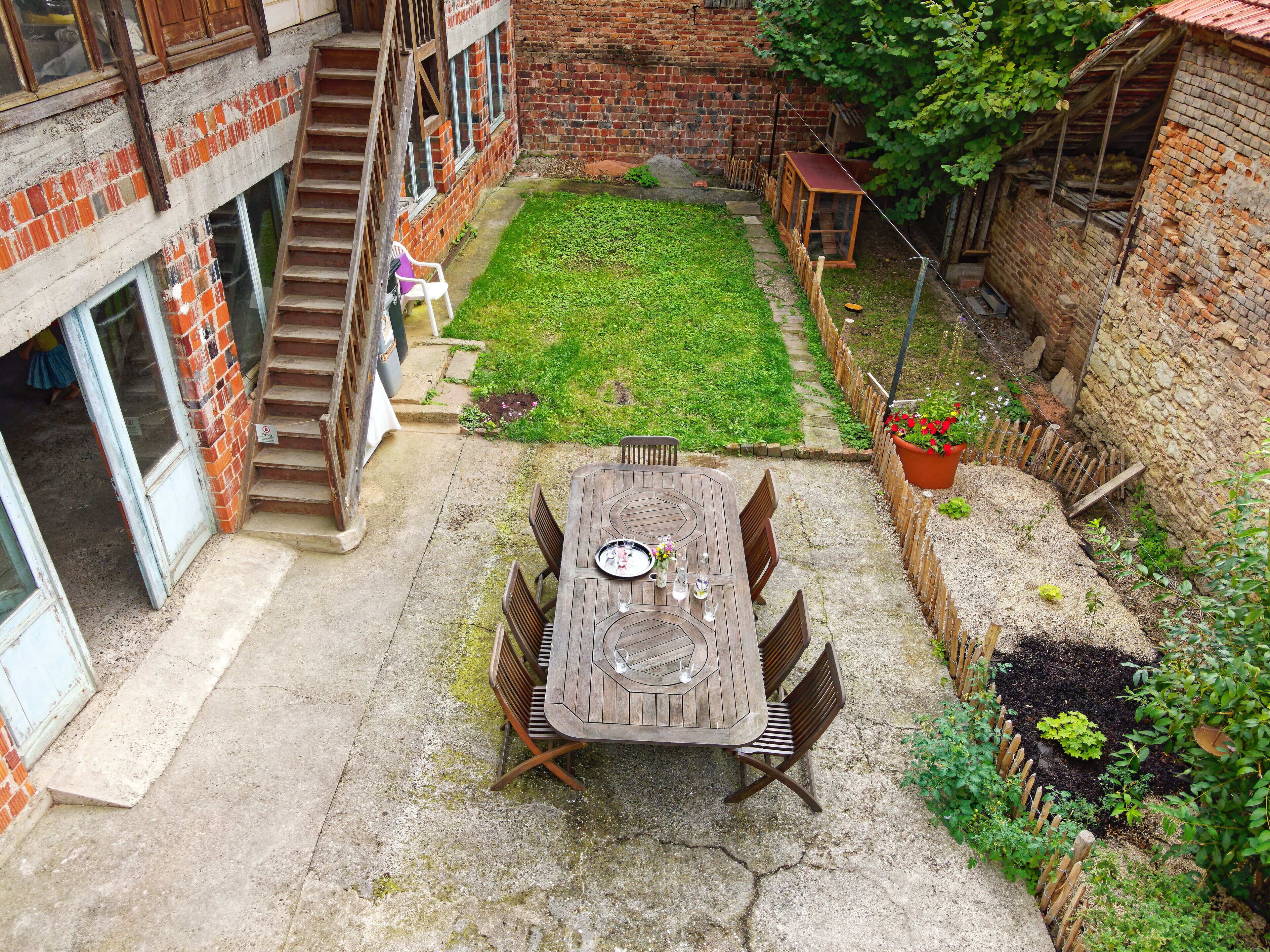 Un patio con una mesa y sillas de madera, un muro de ladrillo y una pequeña zona ajardinada.