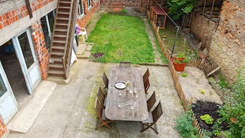 Un patio con una mesa y sillas de madera, un muro de ladrillo y una pequeña zona ajardinada.
