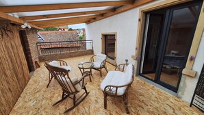 Un patio cubierto con suelo de madera, muebles de mimbre y una puerta de cristal que da a una habitación.