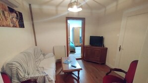 A living room with a sofa, a coffee table, a television on a wooden cabinet, and a door leading to another room. - Cosy house 6-8 people, near Strasbourg, quiet, garden, table tennis, hen (Wingersheim les Quatre Bans)