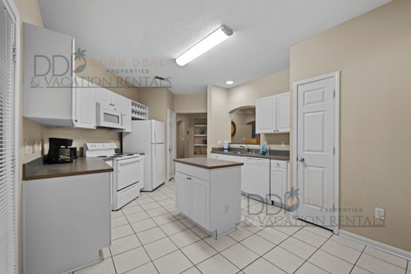 A kitchen with white cabinets, a microwave, a stove, and a coffee maker.