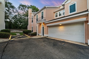 A two-story residential building with a white garage door, a balcony with a black railing, and a well-maintained lawn.