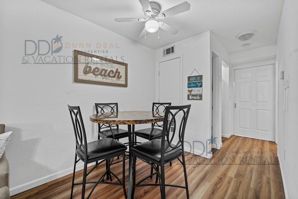 A dining area with a round table and four chairs, a ceiling fan, and a wall-mounted sign.