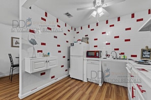 A compact kitchen with white cabinets, a microwave, a refrigerator, and a wooden floor.