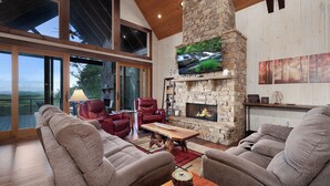 Un salón amplio con chimenea de piedra, sofás de cuero y una gran pantalla de televisión.