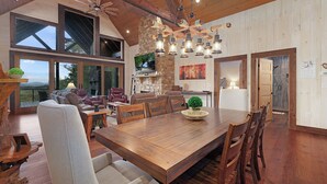 Un comedor espacioso con una gran mesa de madera y sillas, una chimenea de piedra y un televisor montado en la pared.