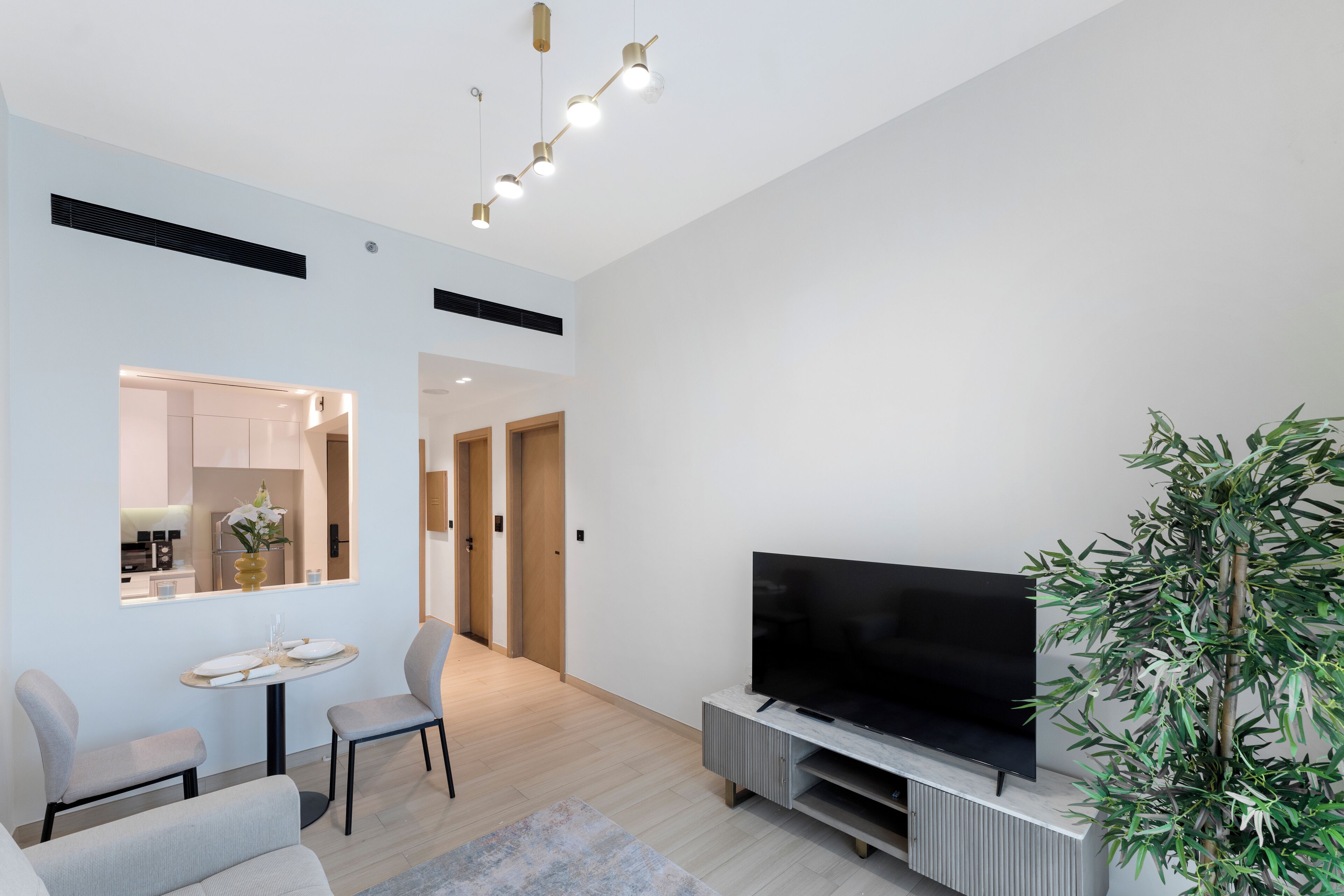 A modern living room with a flat-screen TV, a dining area with a table and chairs, and a large plant.