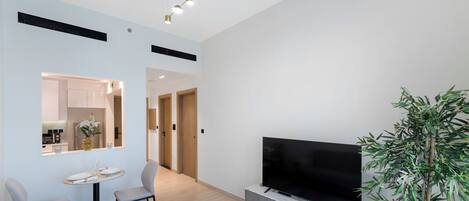 A modern living room with a flat-screen TV, a dining area with a table and chairs, and a large plant.