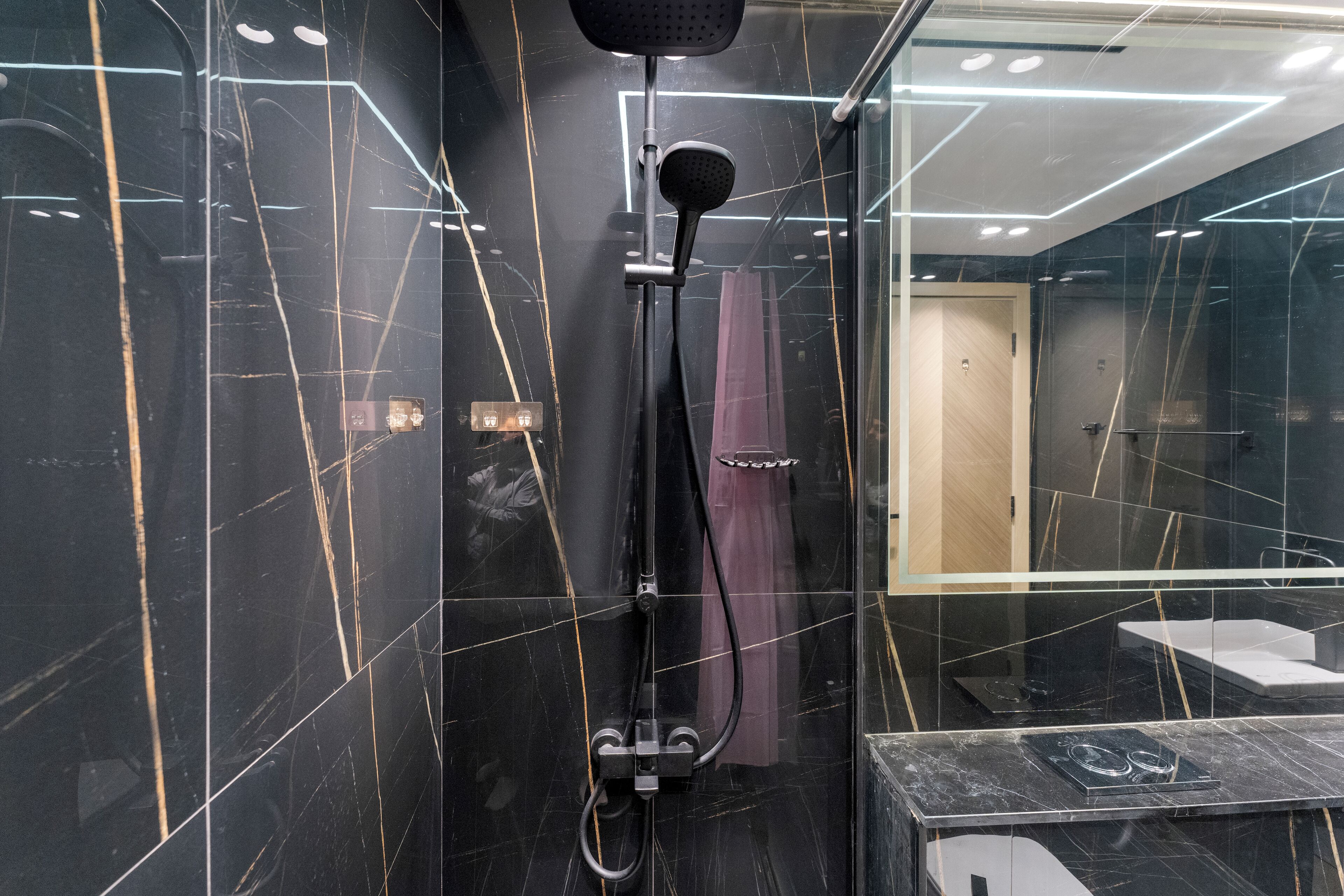 Un baño moderno con ducha de vidrio, paredes de mármol y un inodoro a la vista.