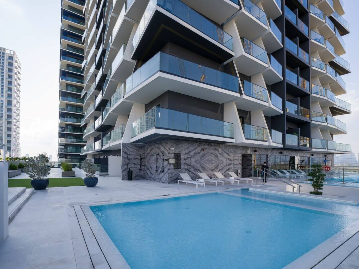 A modern multi-story building with a pool area, featuring a unique architectural design with balconies and a marble facade.