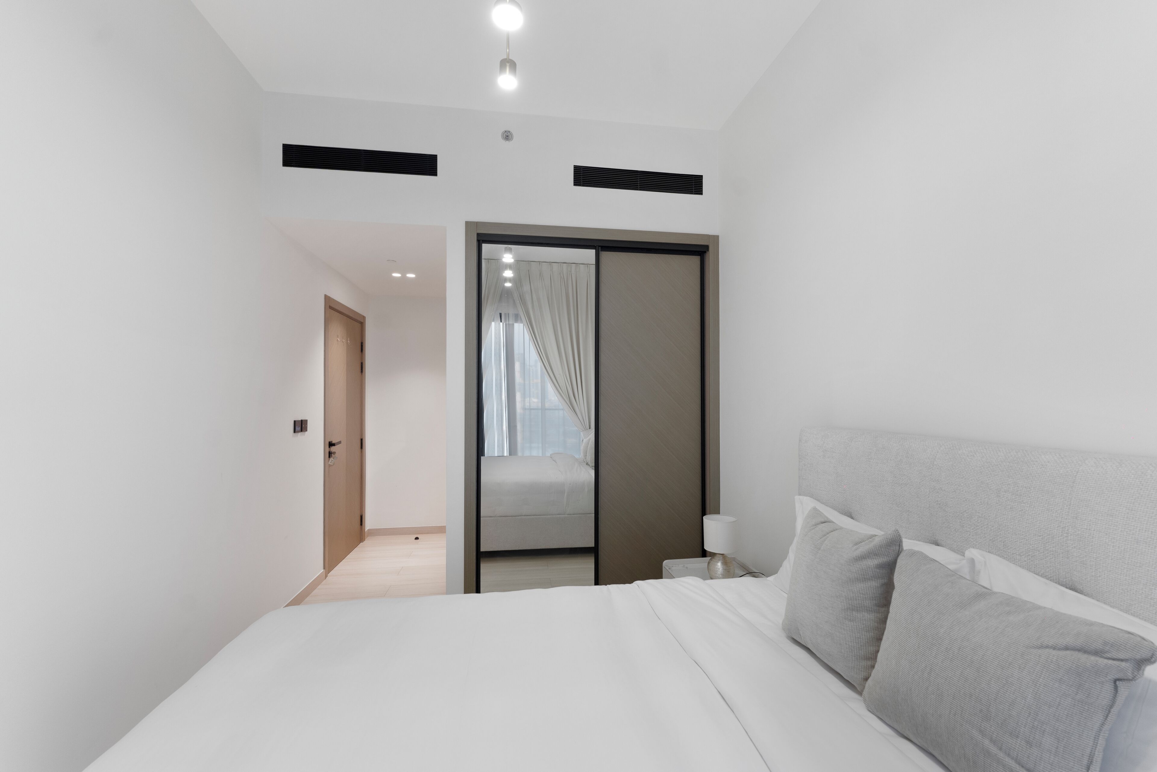 A modern hotel room with a large bed, a bedside table with a lamp, and a sliding door leading to a bathroom.