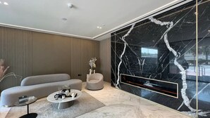 A modern living room with a sofa, armchair, and coffee table, a large black marble wall, and a TV mounted on the wall. - Elegant 1BR Stay in Binghatti Heights (Dubai)