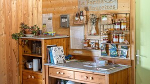 Un interior rústico de madera con un letrero que dice 'La Ferme des Bouteilles', una caja registradora, frascos de conservas y una pequeña planta en la barra.