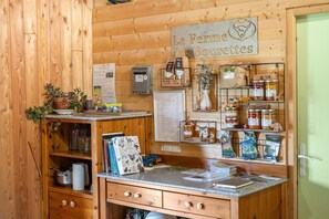 A rustic wooden interior with a sign reading 'La Ferme des Bouteilles,' a cash register, jars of preserves, and a small plant on the counter.