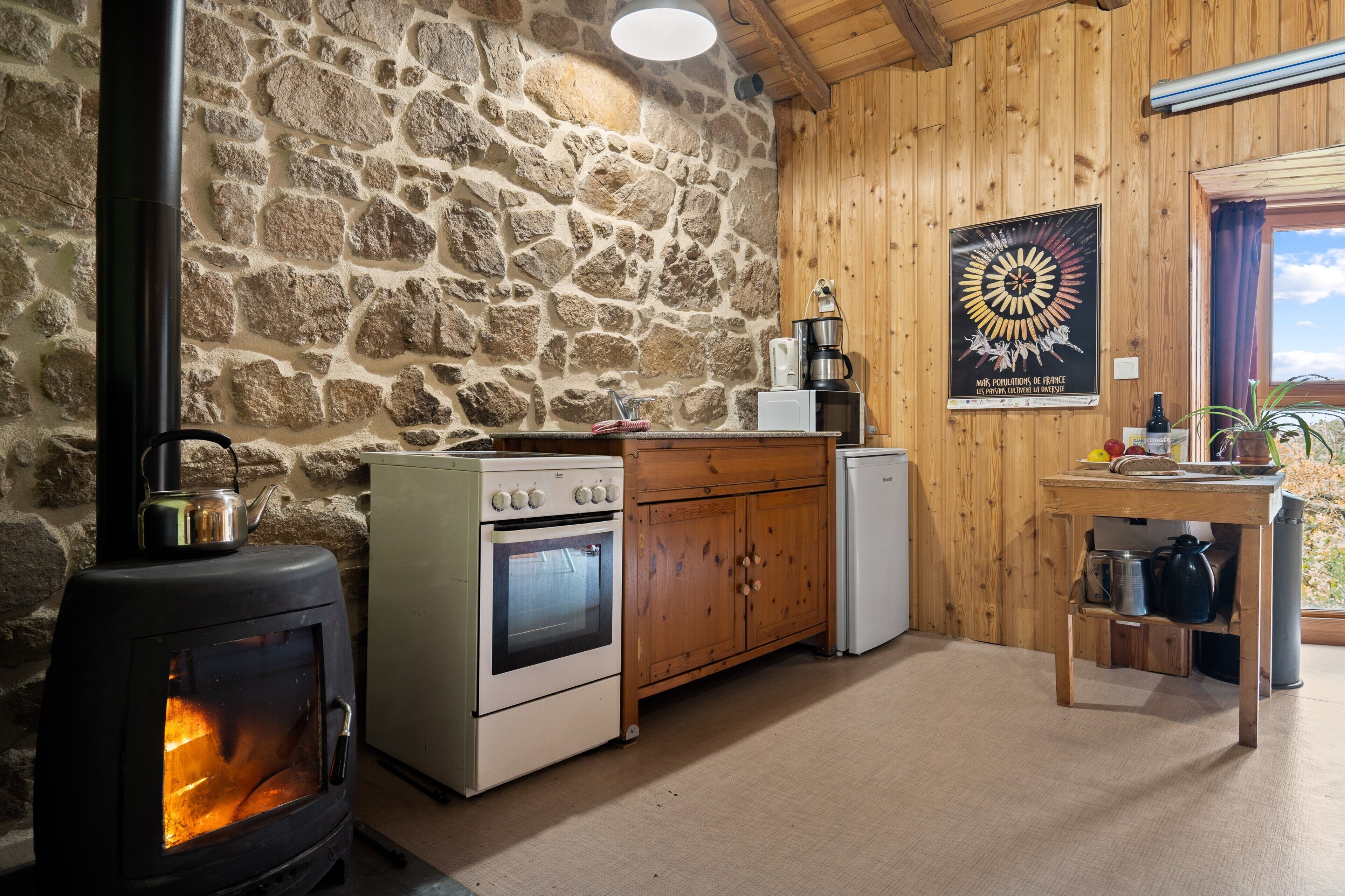 Una cocina rústica con pared de piedra, armarios de madera, estufa y cafetera.