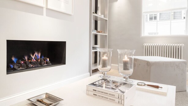 A modern living room with a fireplace, books, and decorative glass vases on a white coffee table. - Prime Knightsbridge Mews-4 bed House (London)