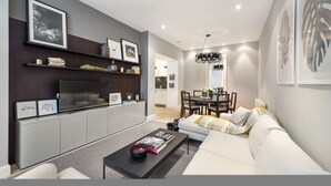 A modern living room with a sofa, coffee table, TV, and shelves with framed pictures. - Prime Knightsbridge Mews-4 bed House (London)