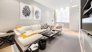 A modern living room with a white sofa, a coffee table, and a bookshelf. - Prime Knightsbridge Mews-4 bed House (London)