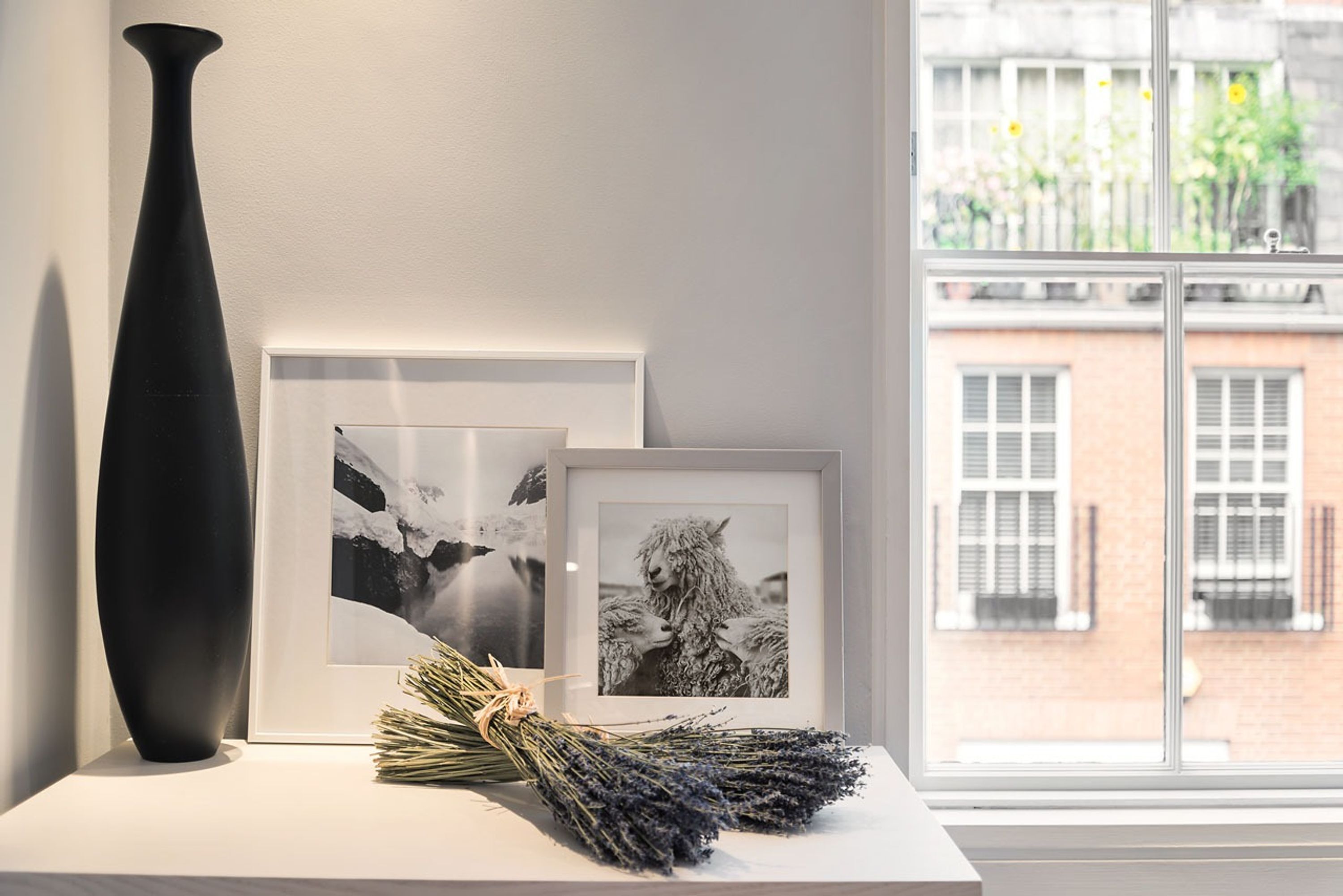 Een zwarte vaas op een witte tafel, naast ingelijste foto's en een bos lavendel.
