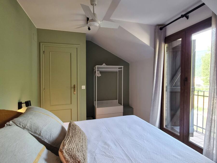 Une chambre à coucher comprenant un lit, un ventilateur de plafond, une fenêtre avec des rideaux, une armoire et un petit balcon.