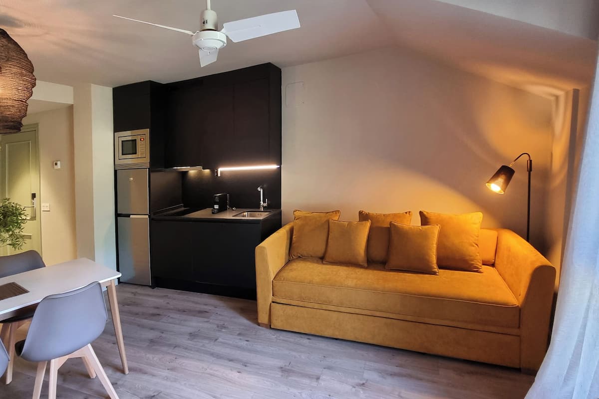 Un espacio habitable compacto con kitchenette, un sofá, una mesa de comedor y un ventilador de techo.