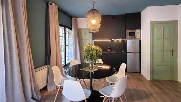 Una cocina moderna con comedor, que presenta una mesa redonda, sillas blancas, una lámpara colgante y una puerta verde.