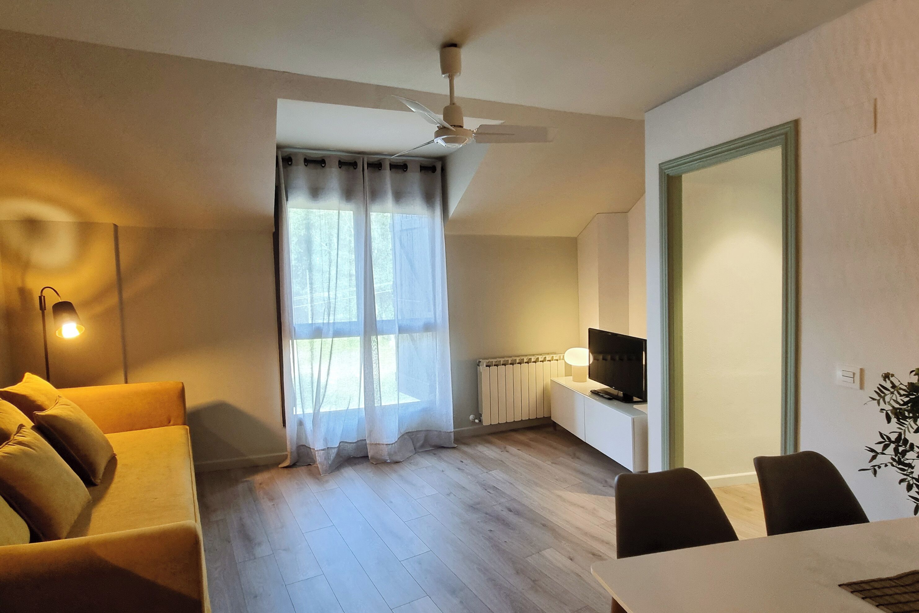 Un salon moderne comprenant un canapé, une table à manger, un téléviseur et un ventilateur de plafond.