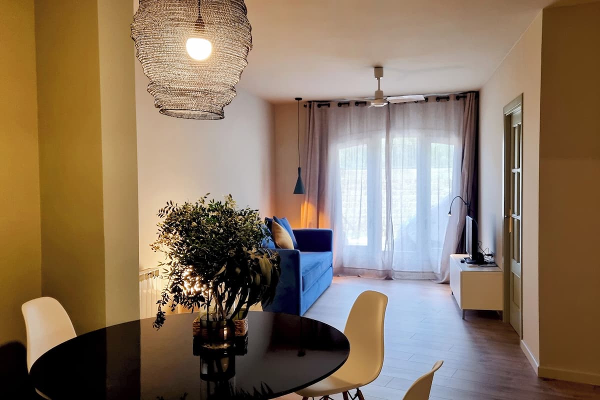 Un comedor con una mesa redonda, sillas y un centro de mesa con planta decorativa.