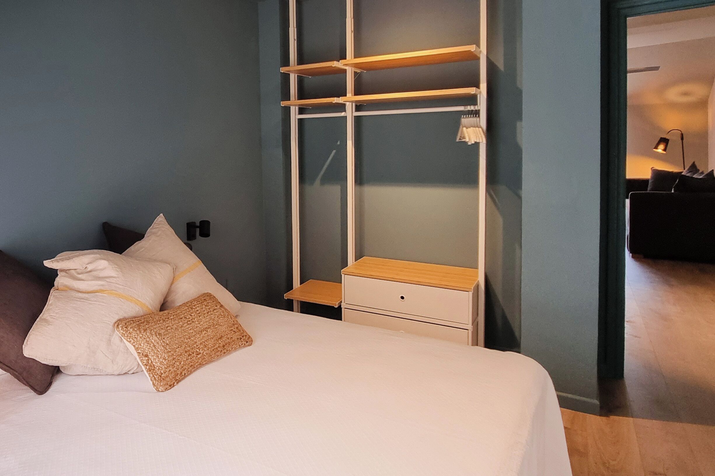 A bedroom with a bed, pillows, a nightstand, a wooden dresser, and a built-in shelving unit.