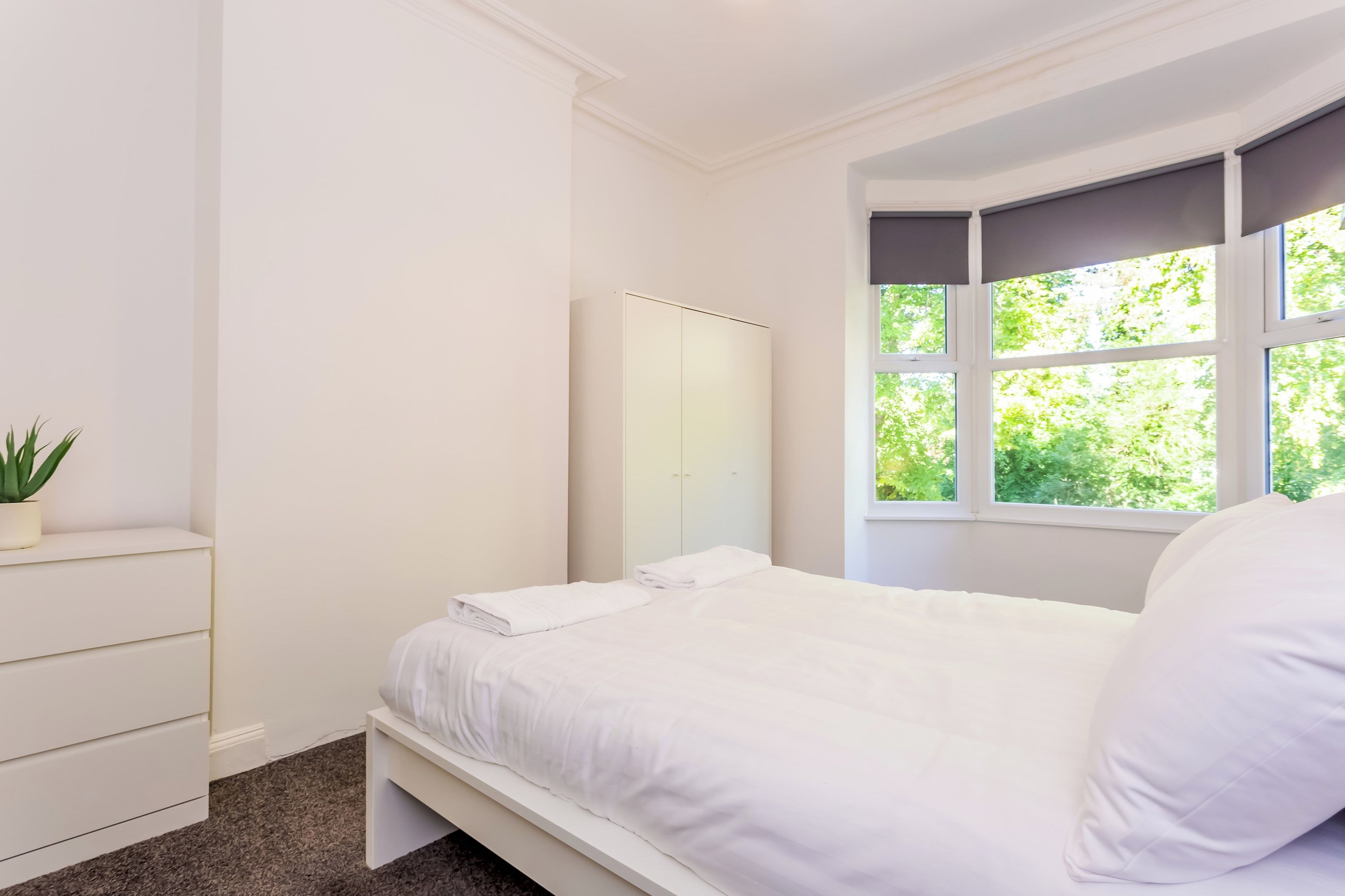 A bedroom with a bed, a dresser, a mirror, and a window with a view of greenery.