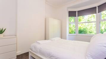 A bedroom with a bed, a dresser, a mirror, and a window with a view of greenery.
